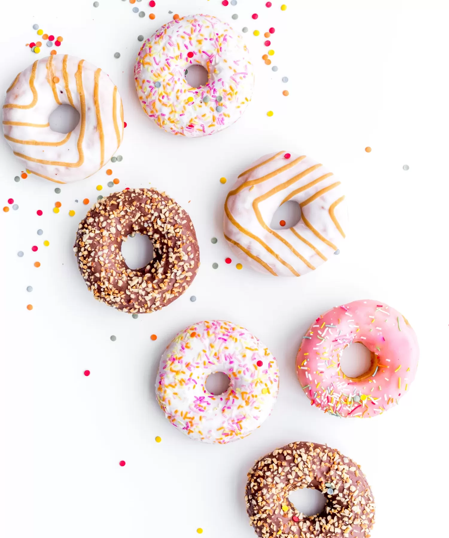 Donuts decorated icing and sprinkles on white background top view copy space pattern